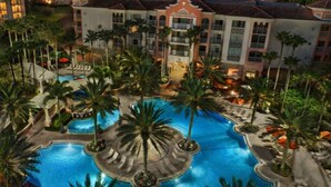 A hotel with a large central pool surrounded by palm trees and lounge areas. -  Family friendly 2-bedroom Full kitchen. Golf ,pools.restaurants,activities. (Orlando)