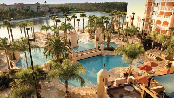 A resort with a large central pool surrounded by palm trees, a separate pool area, and a building with balconies. -  Family friendly 2-bedroom Full kitchen. Golf ,pools.restaurants,activities. (Orlando)