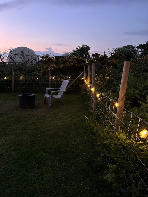 Un jardín con una silla blanca, un bote de basura y luces colgantes.