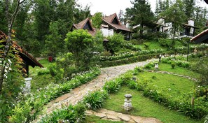 Un jardin avec des allées pavées de pierres, des fleurs blanches et des maisons traditionnelles aux toits de tuiles.