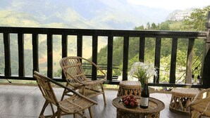 Un balcone con mobili in vimini, un tavolino con una bottiglia e della frutta, e vista sulle montagne.