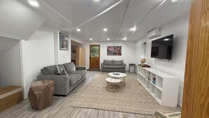 A modern living room with a grey sofa, a coffee table, a bookshelf, and a flat-screen TV mounted on the wall. - Garden Loft with Patios & Green Space · Westchester Retreat (Scarsdale)