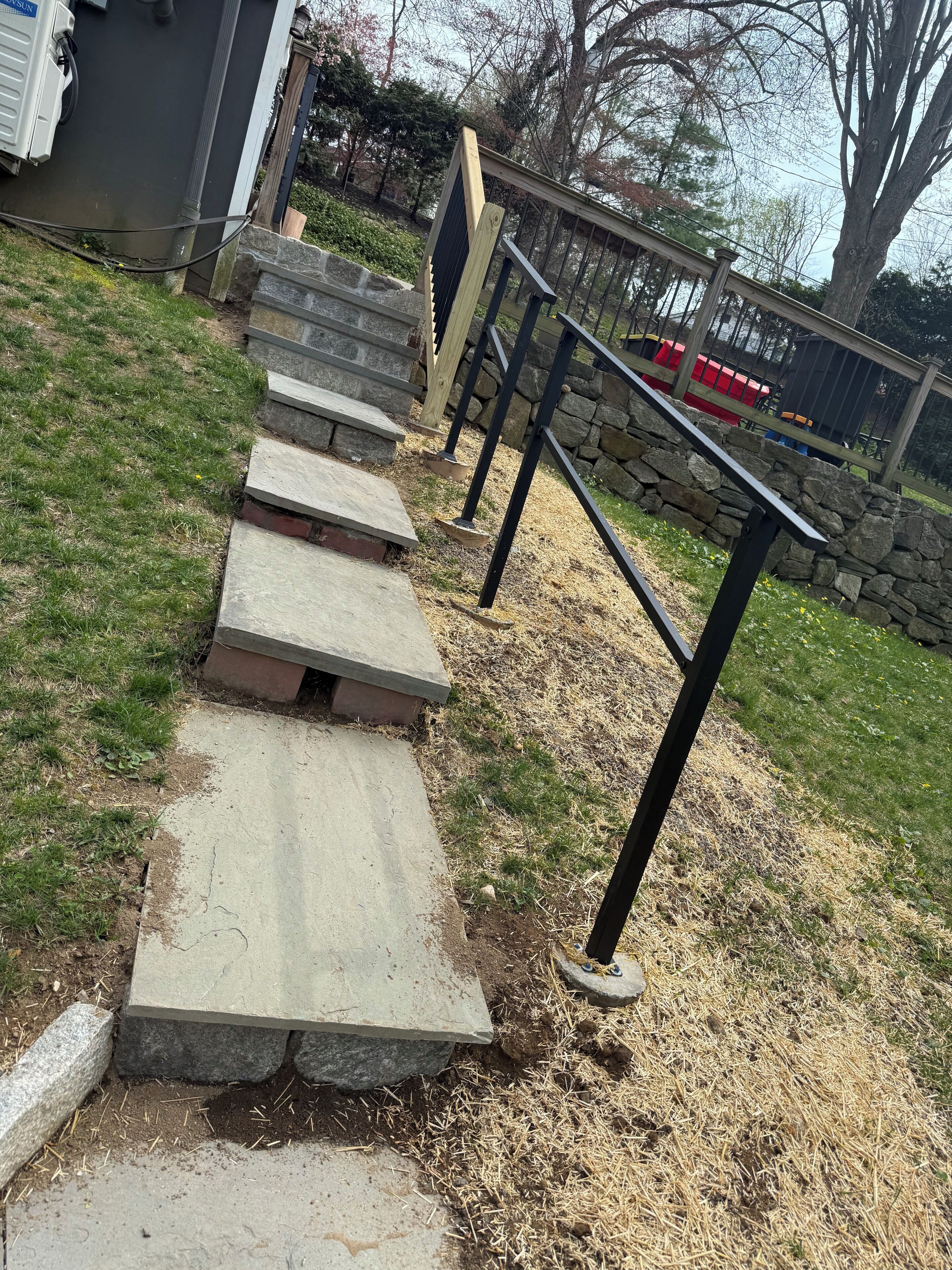 Outdoor stone steps leading to a house with a stone wall and a metal fence.