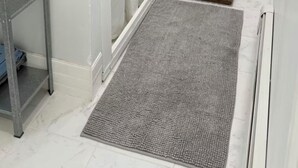 A bathroom with a shower, a metal shelf, a wooden bench, and a grey rug.