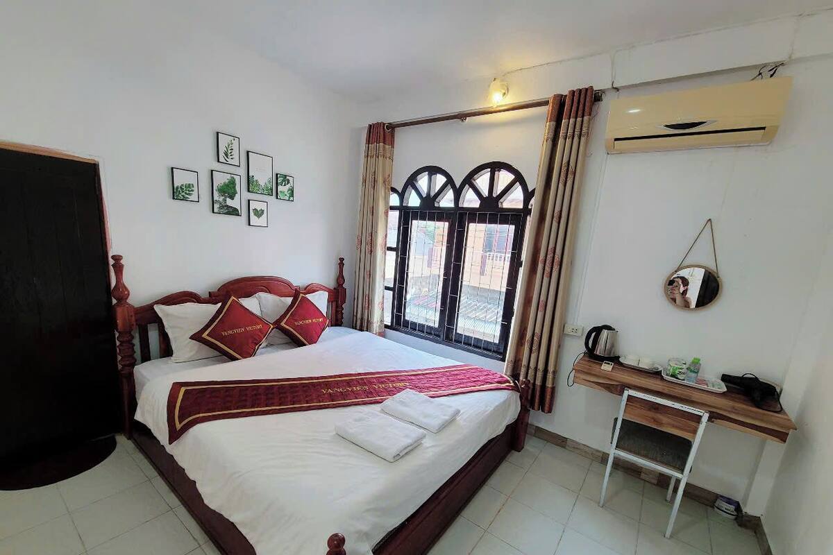 A neatly arranged bedroom with a bed, a desk, and a window with curtains.