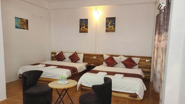 A hotel room with two beds, a small round table, two black chairs, and artwork on the walls. - VANG VIENG VICTORY HOSTEL  (Vang Vieng)