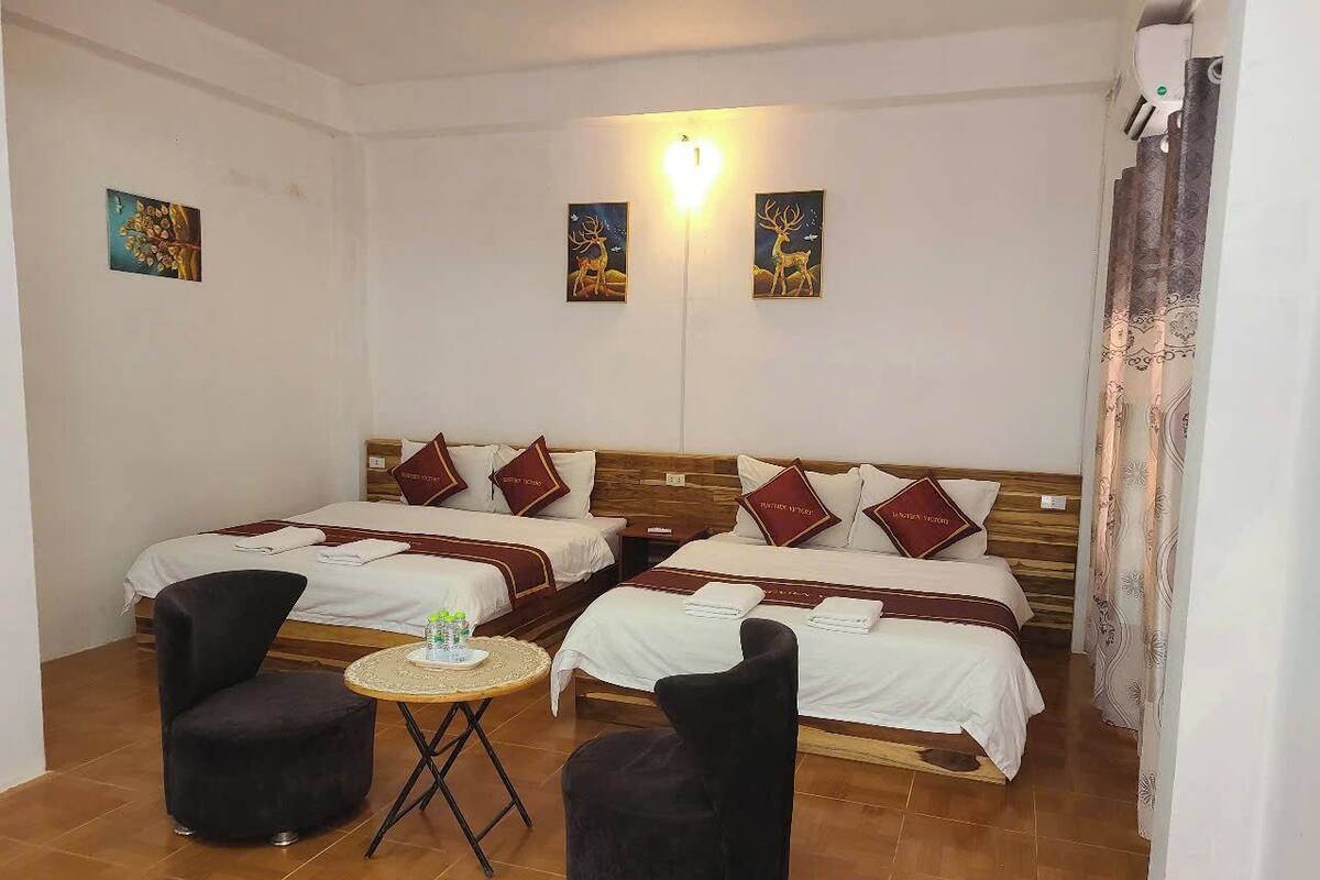A hotel room with two beds, a small round table, two black chairs, and artwork on the walls.