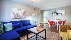 Een woonkamer met een blauwe bank, een salontafel en een eethoek met rode stoelen.