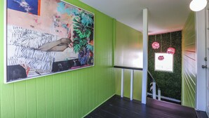 Een hal met groene muren, een groot abstract schilderij en een trap met een groene wand en een klein raam met een krans.