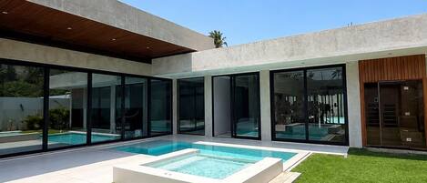 A modern house with a swimming pool, large glass windows, and a well-maintained lawn.