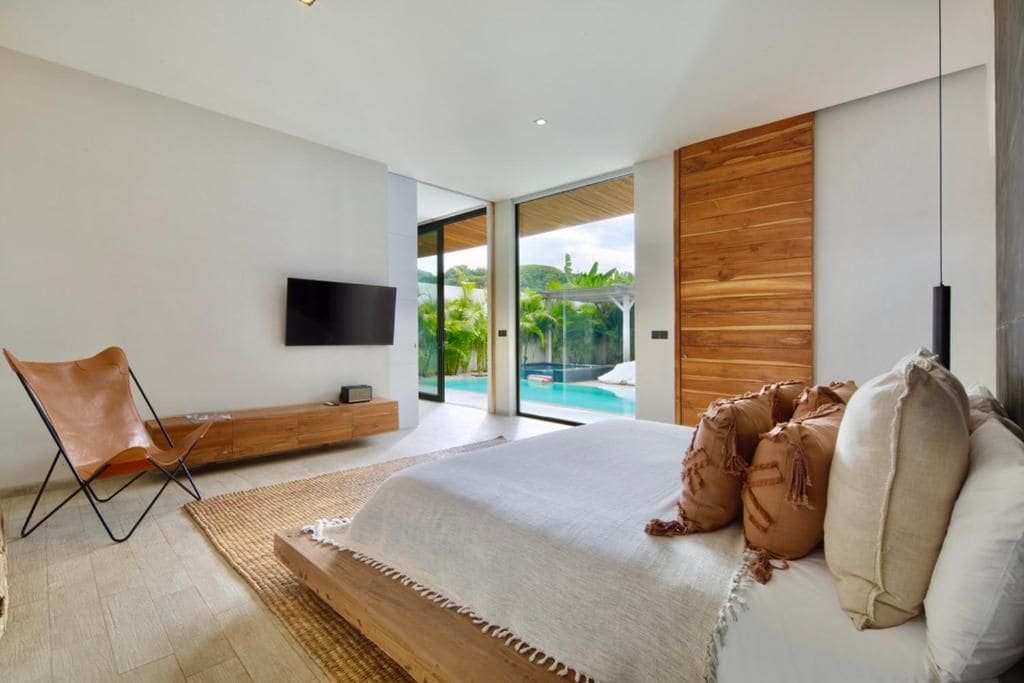 A modern bedroom with a large bed, a television, and a view of a swimming pool.