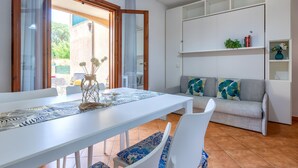 A modern living room with a white sofa, a dining table with chairs, and a kitchen area.