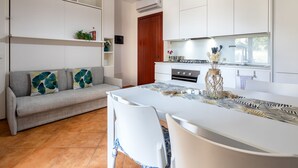 A modern kitchen with white cabinets, a grey sofa, and a dining table with chairs.