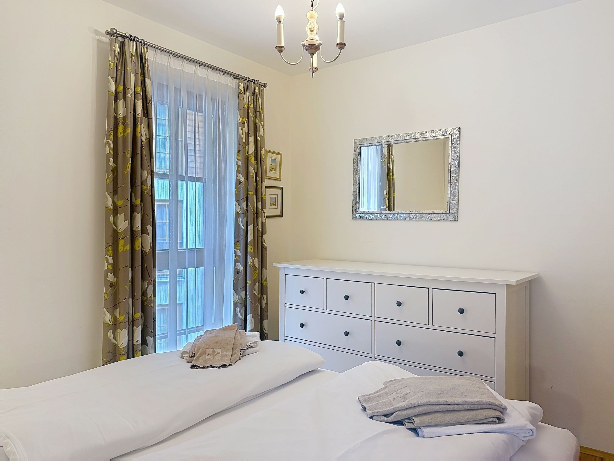 Une chambre à coucher avec un lit, une commode, un miroir et un lustre.