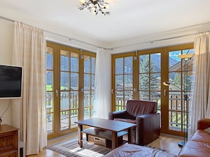 A room with a large sliding glass door, a wooden table, a leather chair, a sofa, a TV, and a floor lamp.