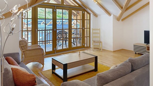 A spacious room with a high ceiling, wooden beams, a large sliding glass door leading to an outdoor area, a sofa, a coffee table, and a television. - SMR Family comfort (incl. SPA) by Interhome (Rauris)