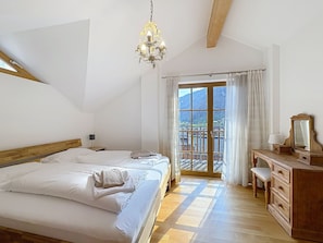 A bedroom with two beds, a chandelier, a dresser, and a view of mountains through a large window.