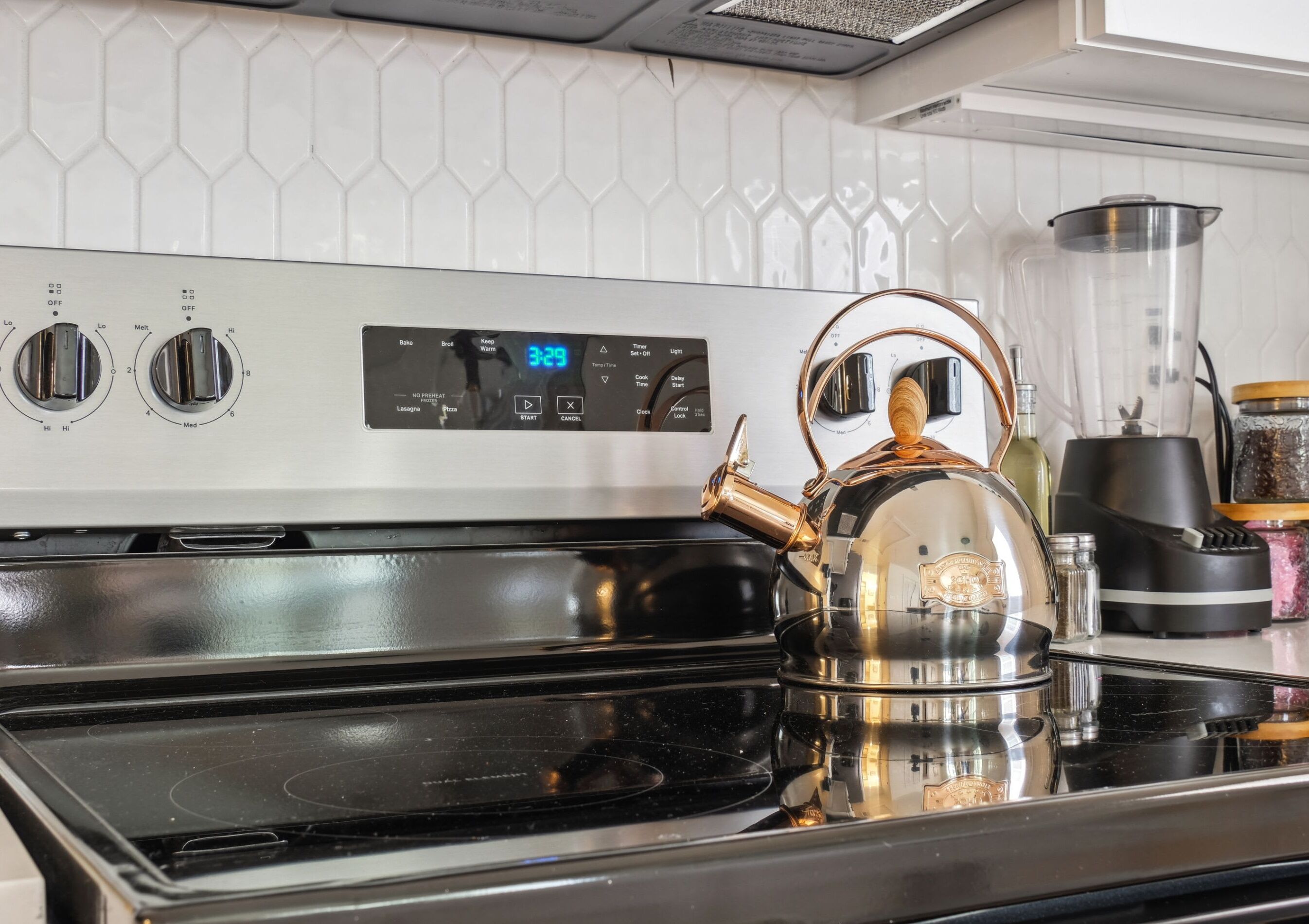 A kitchen with a stainless steel stove, a kettle, and a digital clock displaying 3:29.