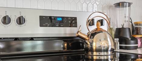 A kitchen with a stainless steel stove, a kettle, and a digital clock displaying 3:29.