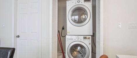 A laundry room with two stacked washing machines, a door, and a broom.