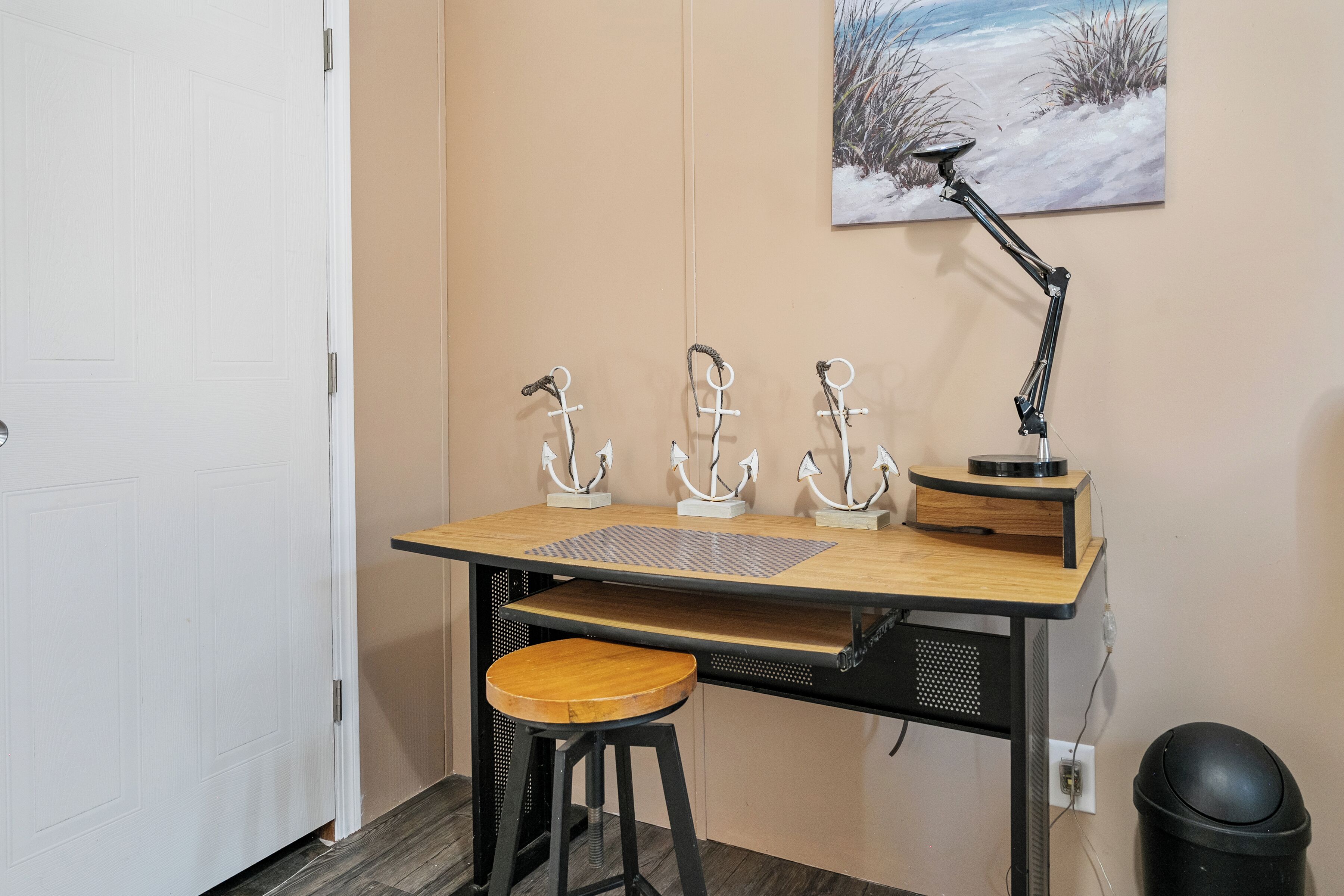 Un petit espace de travail bien rangé, avec un bureau en bois, trois crochets métalliques fixés au mur, une lampe de bureau noire et une poubelle noire.