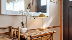 Une pièce avec une table en bois, un vase blanc contenant une plante, une lampe dorée et un grand miroir qui reflète la pièce.