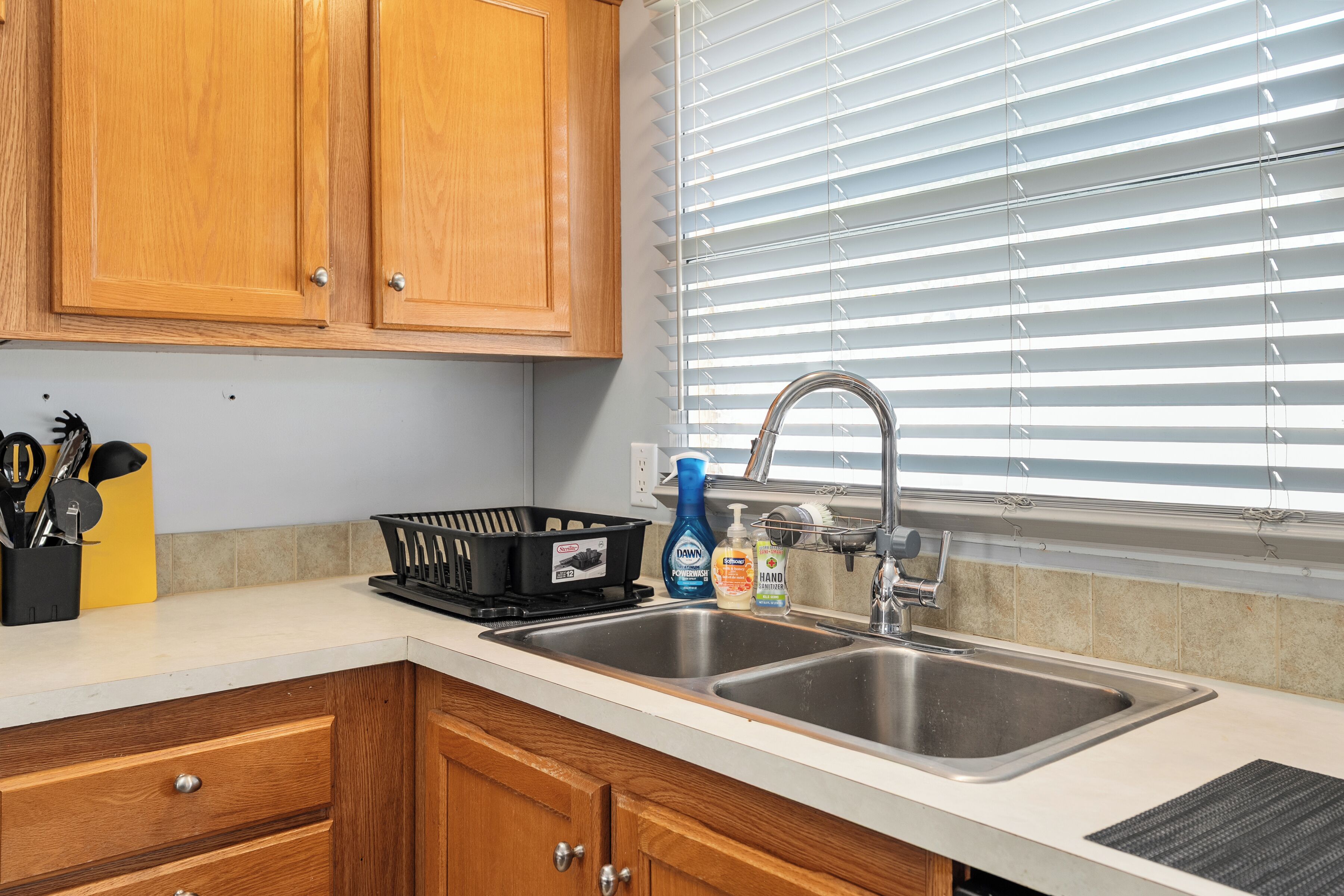 A kitchen with wooden cabinets, a double sink, and a window with blinds.