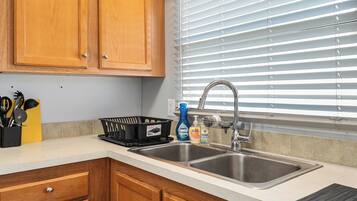 A kitchen with wooden cabinets, a double sink, and a window with blinds.