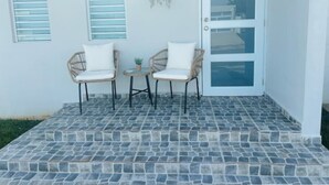 A patio with two wicker chairs and a small table, a hanging plant, and a door with glass panels. - Peaceful Hideaway in Cabo Rojo (Boquerón)
