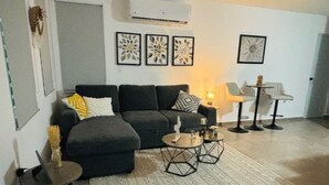 A living room with a dark grey sofa, a patterned rug, and a coffee table with decorative items. There are wall-mounted air conditioning units and framed artwork above the sofa. - Peaceful Hideaway in Cabo Rojo (Boquerón)