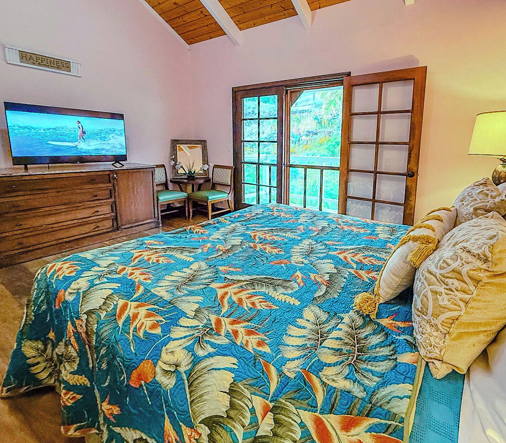 Een slaapkamer met een bed, een televisie op een dressoir, een stoel en een raam met uitzicht op groen.