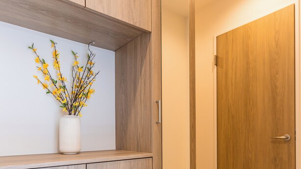 Ein modernes Interieur mit Holzschränken, einer weißen Vase mit gelben Blumen und einer Holztür.