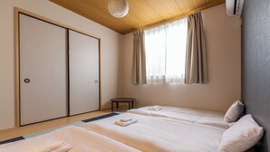 Ein Hotelzimmer mit zwei Betten, einem kleinen runden Tisch, einer Schiebetür und einem Fenster mit Vorhängen.