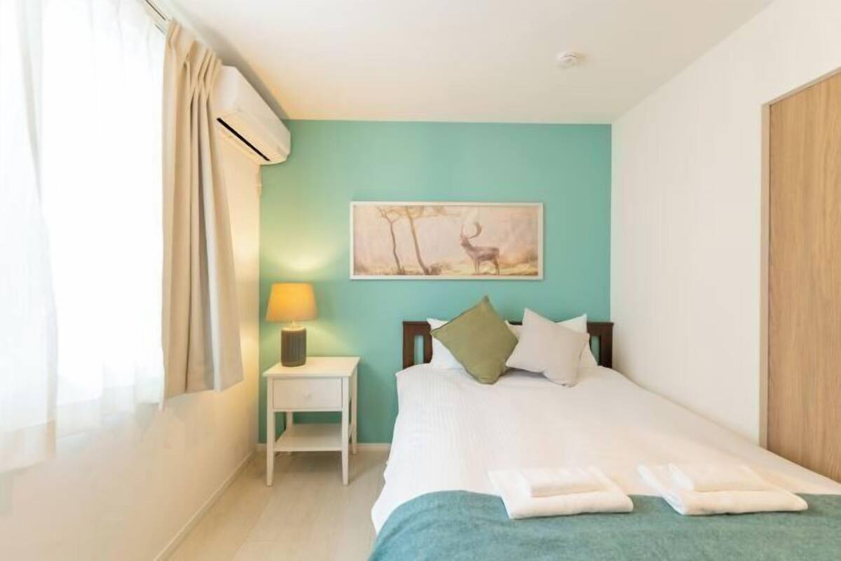 A bedroom with a bed, a nightstand, a lamp, a painting, and a window with curtains.