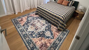 Un dormitorio con cama, una alfombra, una ventana con cortinas y un equipo de aire acondicionado.