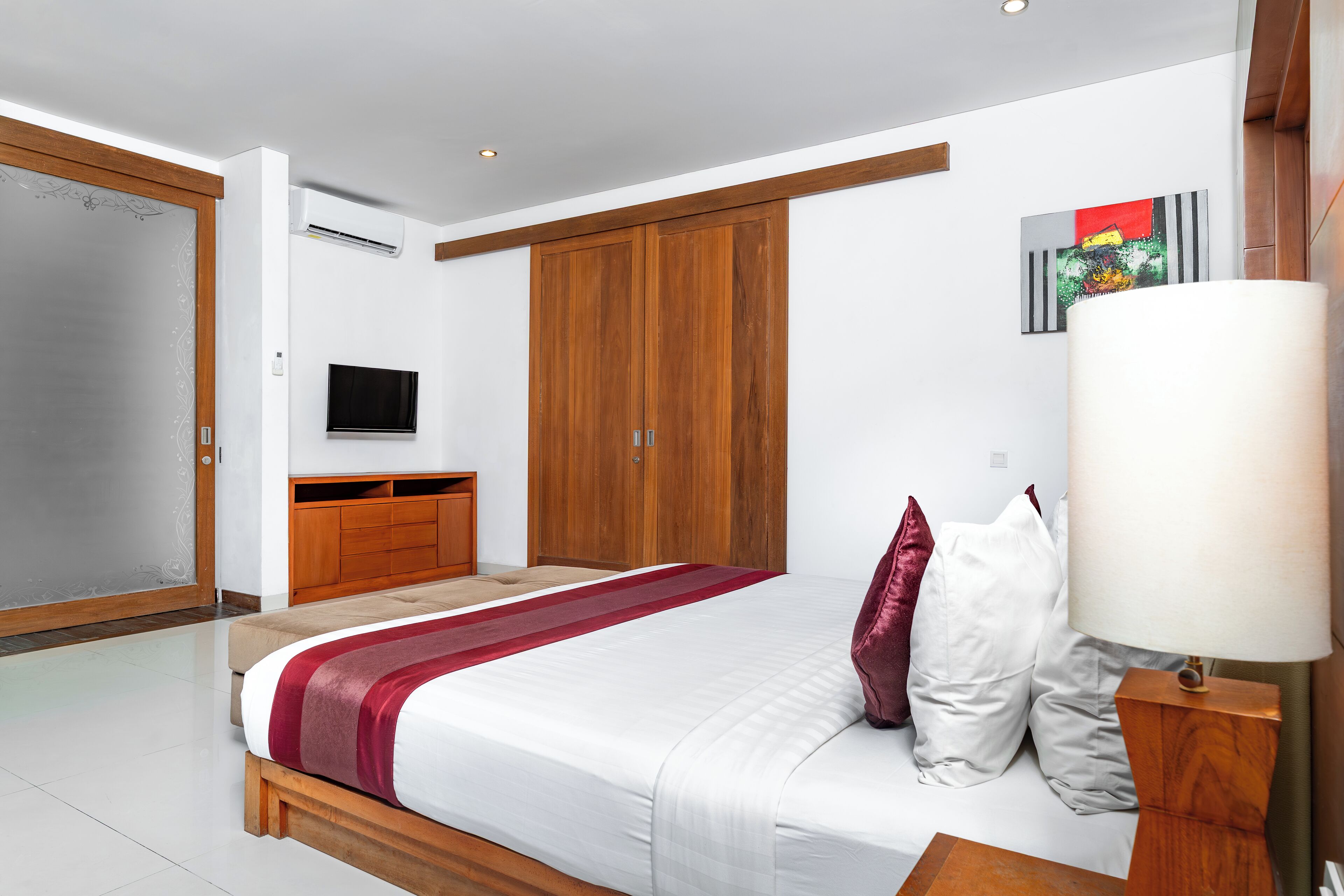 A modern bedroom with a large bed, wooden wardrobe, and a television on a stand.
