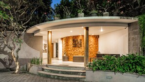 Un edificio moderno con una entrada curva, un interior con paneles de madera y una zona de estar con banco y mesa.