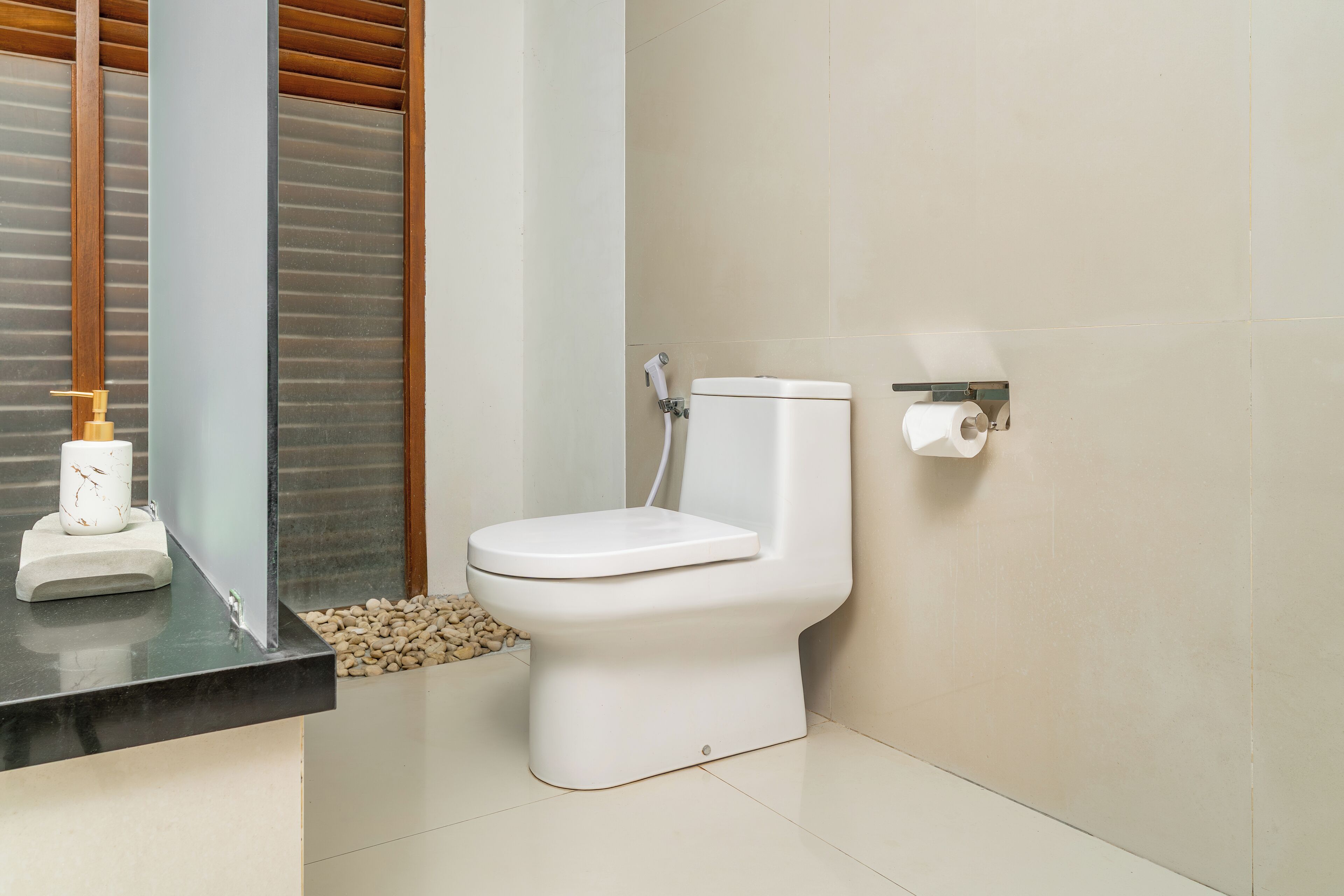 A modern bathroom with a toilet, a hand soap dispenser, and a toilet paper holder on the wall.