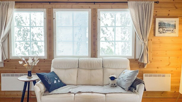 Una habitación acogedora con un sofá blanco, una mesita con un florero y tres ventanas con persianas.