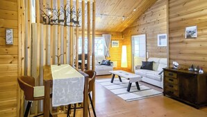 Interior de una cabaña de madera con una mesa de comedor, sillas, un sofá y un mueble bajo.