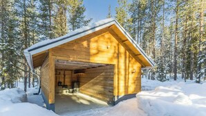 Una cabaña de madera con techo inclinado, rodeada de nieve y árboles.