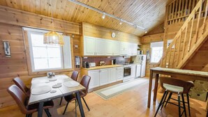 Un interior de madera con una mesa de comedor, sillas, una cocina con armarios blancos y una escalera.