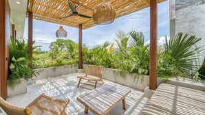 A covered outdoor seating area with a ceiling fan, wicker furniture, and a view of lush greenery.