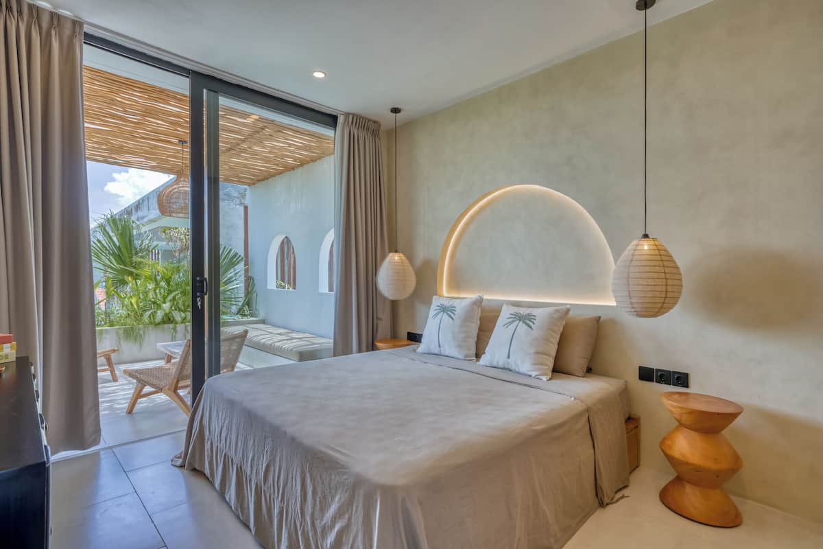A modern bedroom with a large bed, a wooden side table, and a view of a balcony with outdoor furniture.