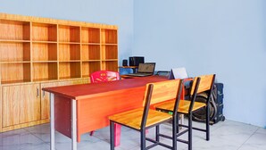 Una habitación con un escritorio de madera, dos sillas, una computadora portátil, una silla roja y una estantería.