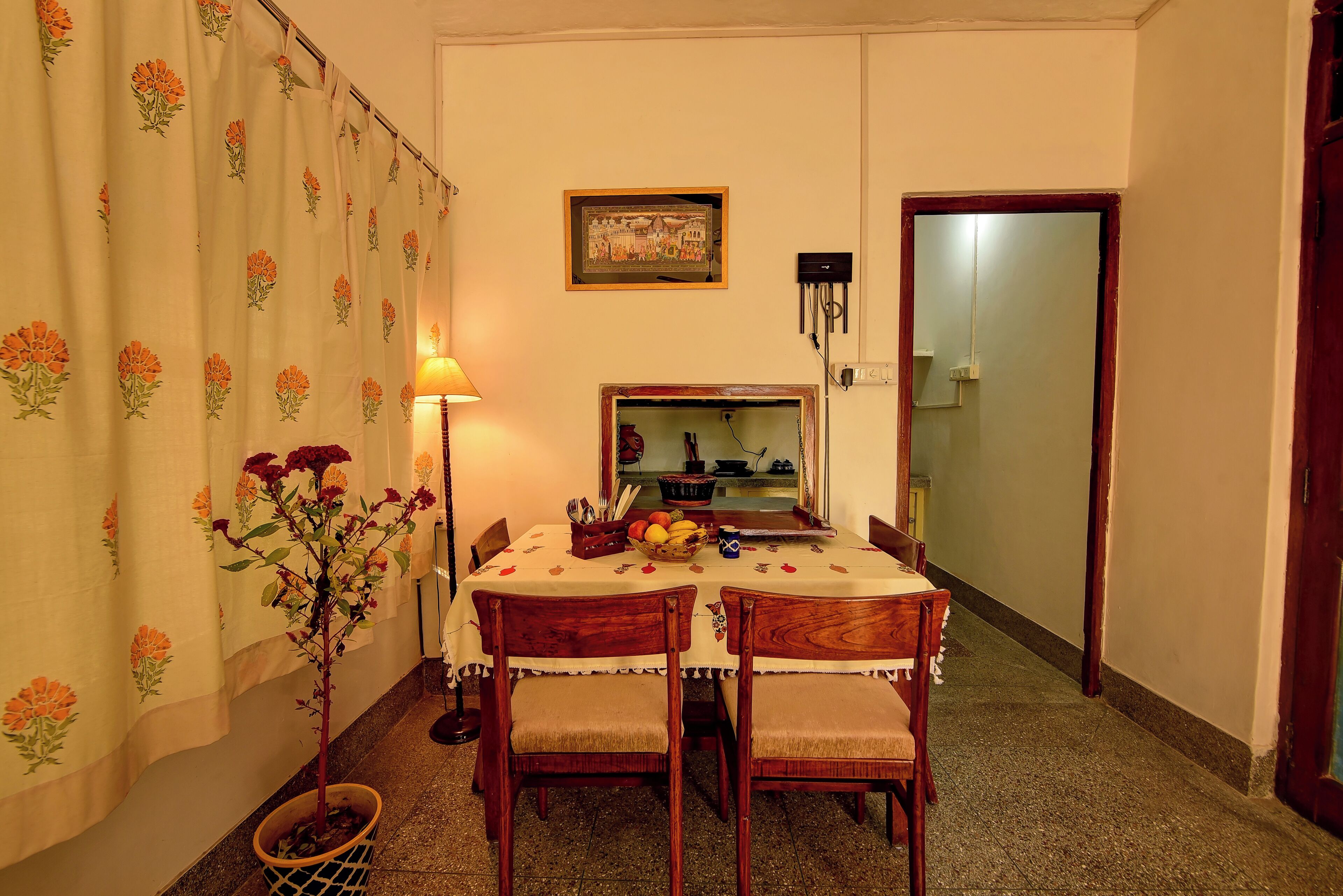 A dining area with a table set for two, a potted plant, and a wall-mounted clock.