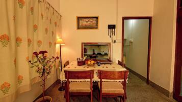 A dining area with a table set for two, a potted plant, and a wall-mounted clock.