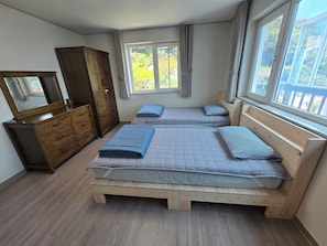 Une chambre avec deux lits, une commode en bois, un miroir et une fenêtre avec des rideaux.