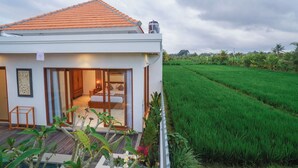 A modern house with a tiled roof, a bedroom with a bed and a nightstand, and a view of a green field.