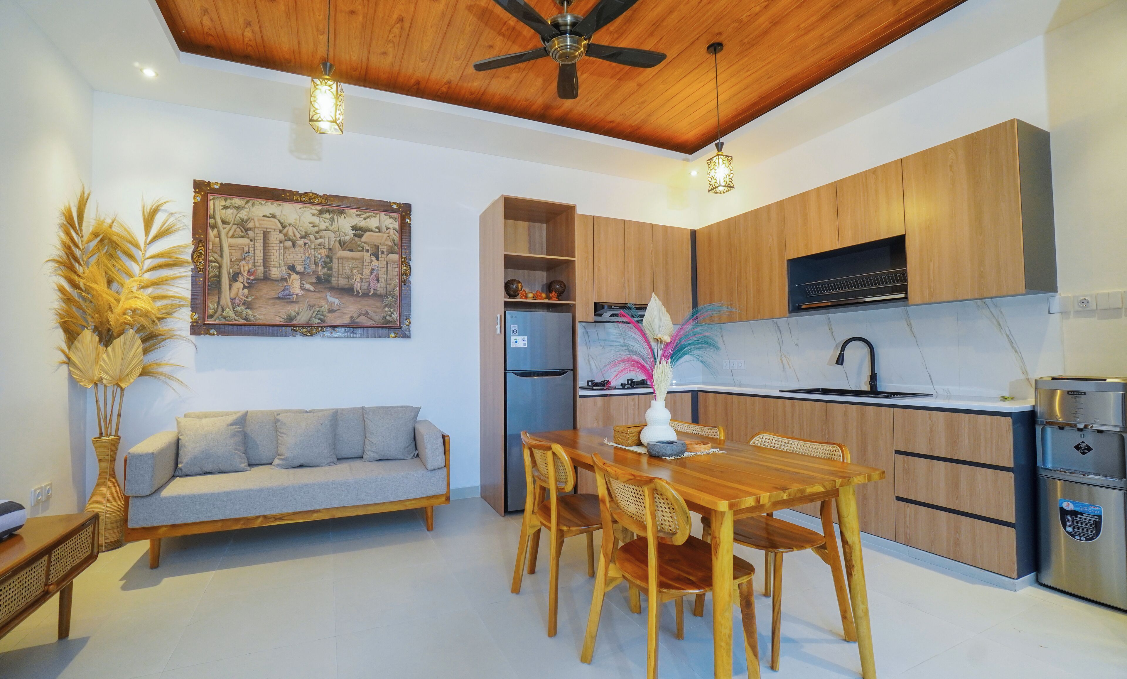 Una cucina moderna con mobili in legno, piano cottura integrato e frigorifero. C'è un'area pranzo con tavolo e sedie in legno e un divano nel soggiorno.